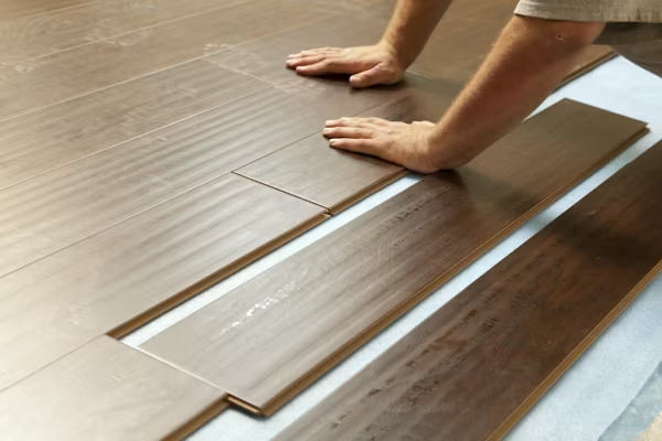 A man installs wood flooring, focusing on precise placement and alignment in a spacious room.