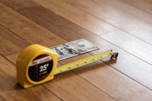 Money and a tape measure on wooden flooring, symbolizing installation costs.